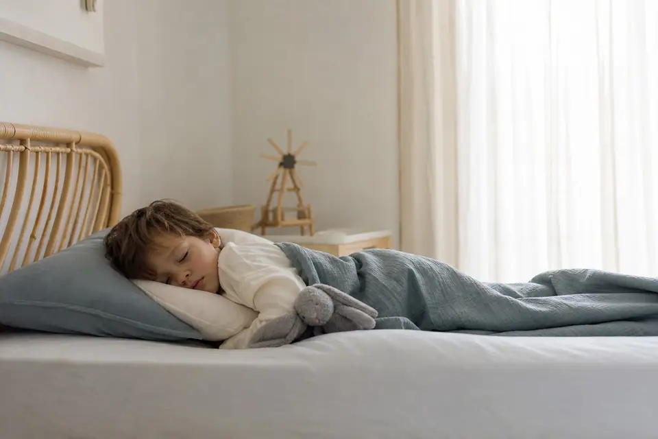 Jeune enfant endormi sur un petit lit dans une chambre calme, lumière douce d’après-midi