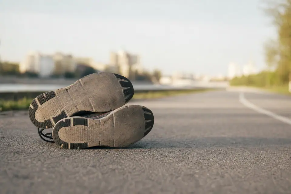 Paire de chaussures de running usées posée sur le bitume, semelle extérieure lisse au niveau de l’avant-pied