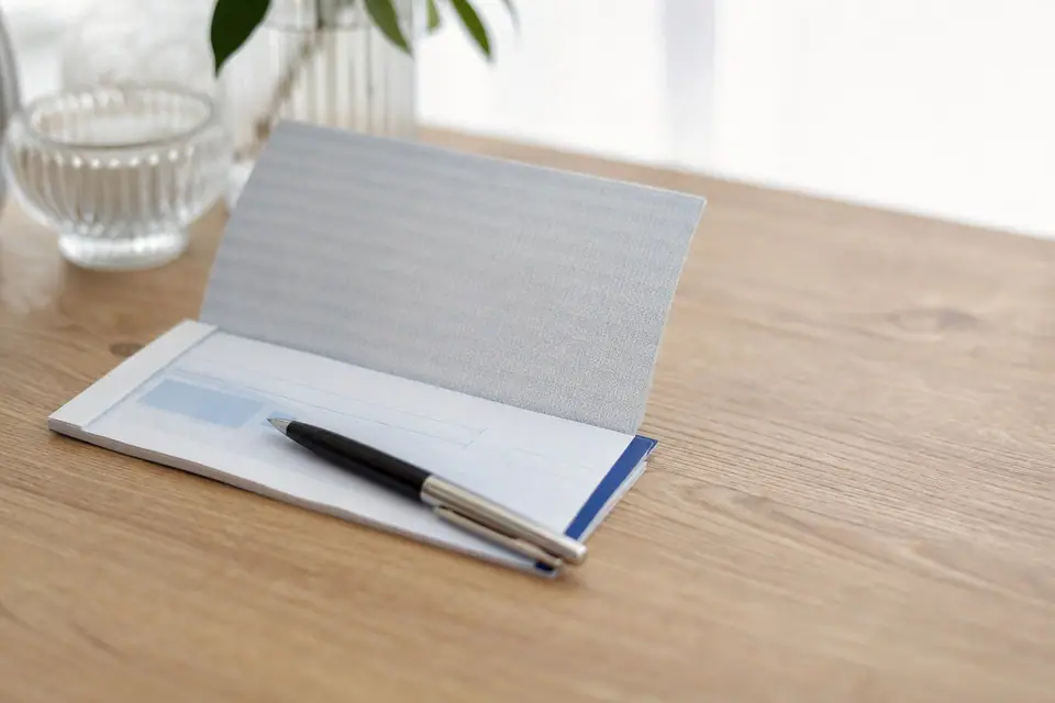 Chéquier et stylo posés sur une table, chèque partiellement rempli en arrière-plan