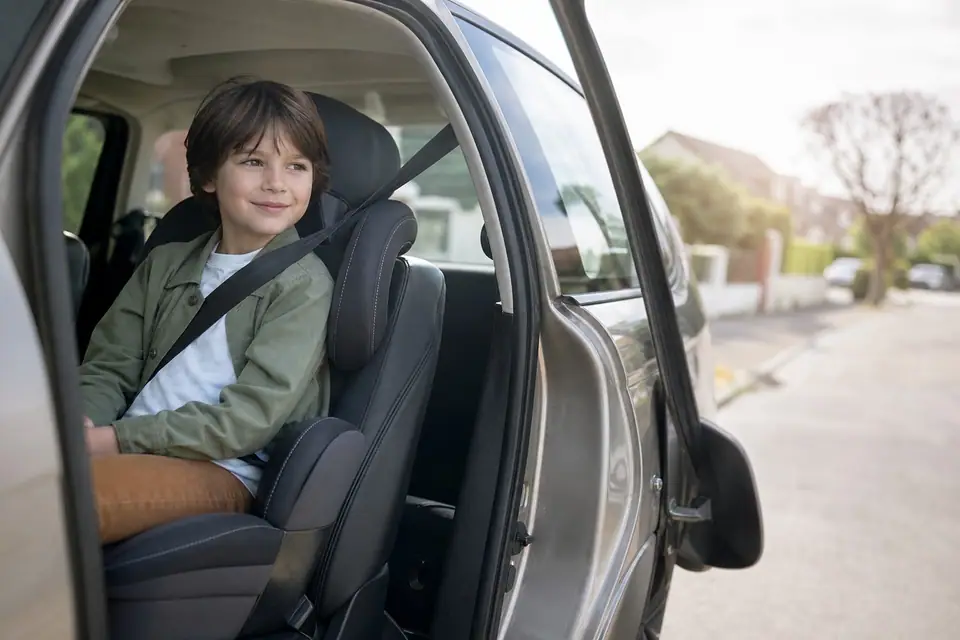 Enfant assis dans un rehausseur avec dossier à l’arrière d’une voiture, ceinture passée sur l’épaule
