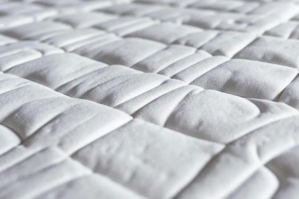 Matelas blanc déhoussé dans une chambre aérée avec protège-matelas et linge de lit propre