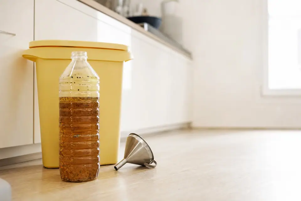Bouteille en plastique remplie d’huile de friture usagée posée à côté d’une poubelle de tri