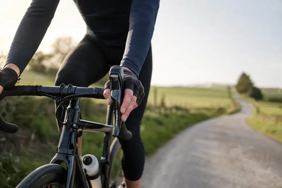 Cycliste tenant son guidon, mains gantées, sur une route de campagne