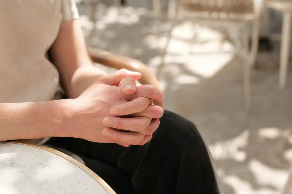 Mains jointes et légèrement rougies tenues par une personne assise dehors en été