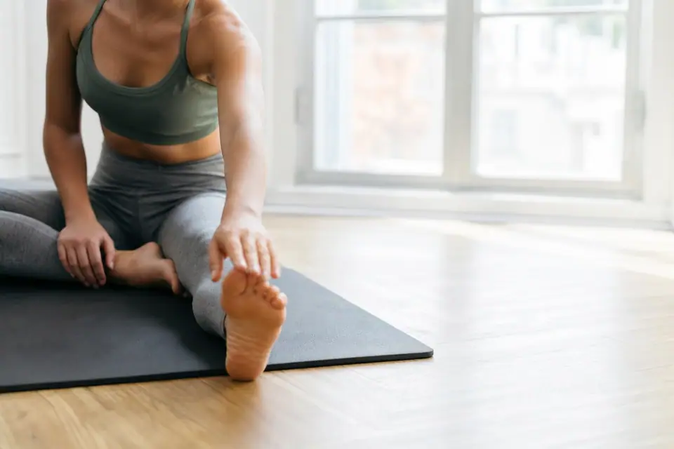 Personne s’étirant les jambes après une séance de sport, tapis au sol, lumière du matin