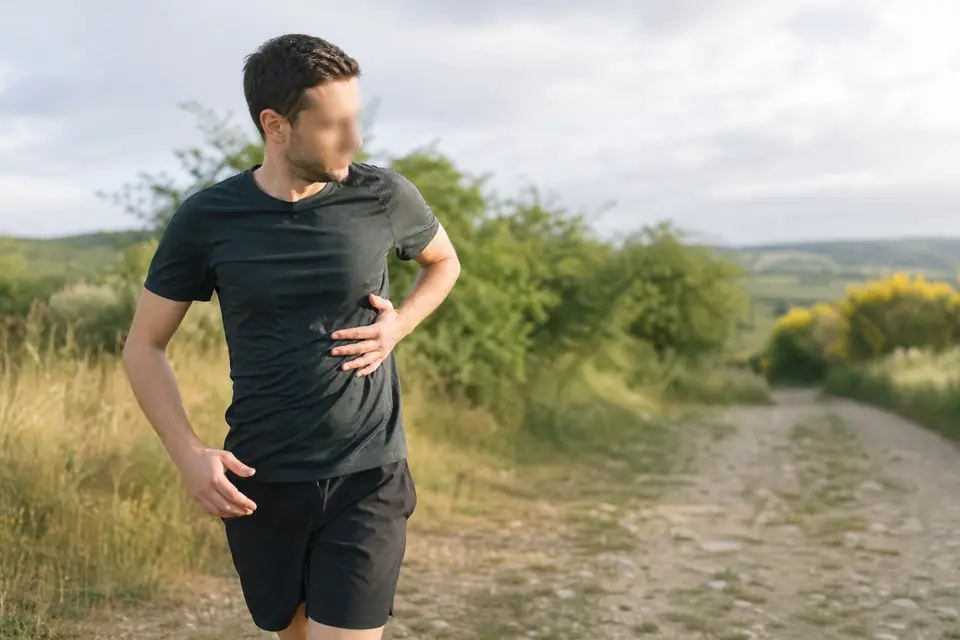 Coureur en extérieur portant la main sur le côté du buste, en pleine course sur un chemin