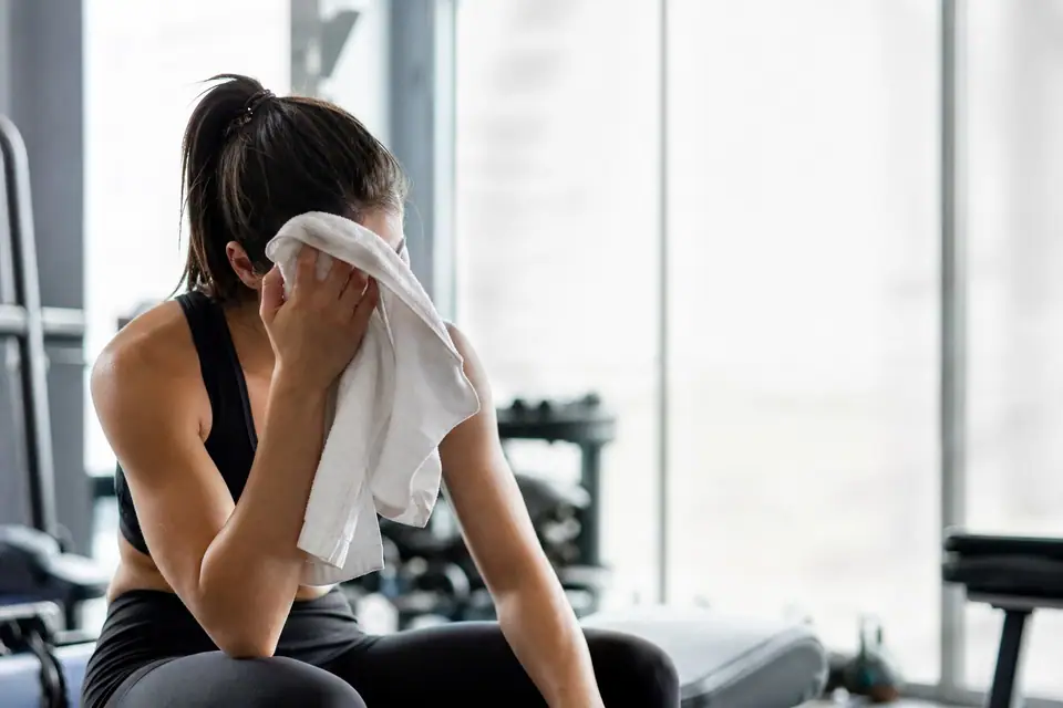Personne en tenue de sport s’essuyant le front avec une serviette après un entraînement