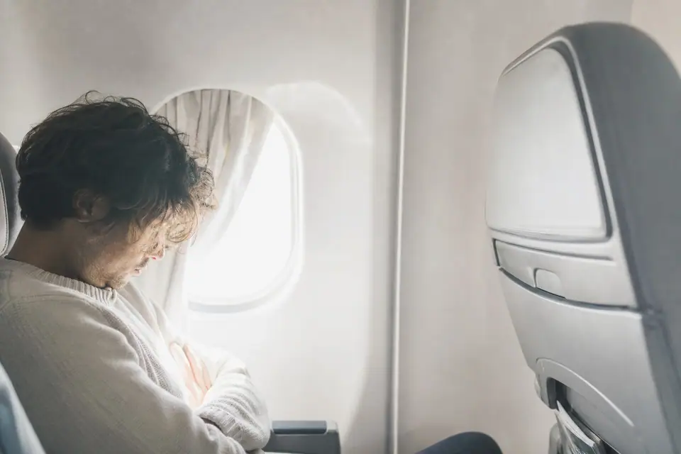 Voyageur somnolent assis près d’un hublot d’avion, lumière du jour filtrant à travers le rideau