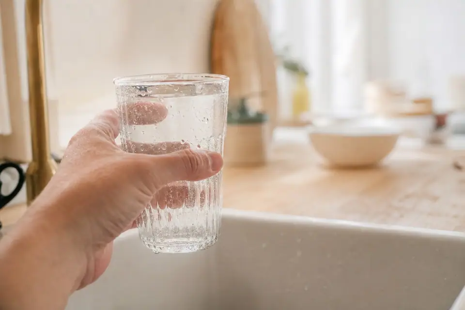 Verre d’eau du robinet rempli sous un robinet de cuisine, lumière naturelle d’été