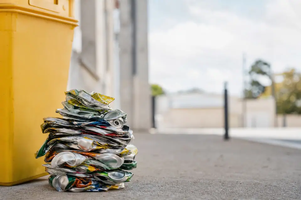 Canettes en aluminium écrasées empilées près d’un bac de tri jaune