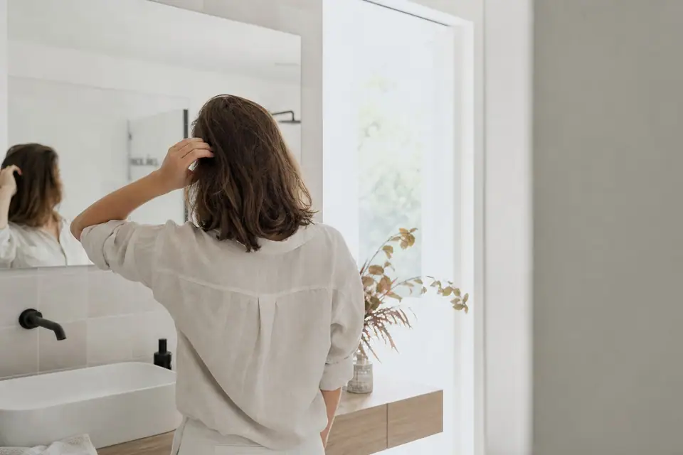 Personne se coiffant devant un miroir dans une salle de bain lumineuse, cheveux mi-longs