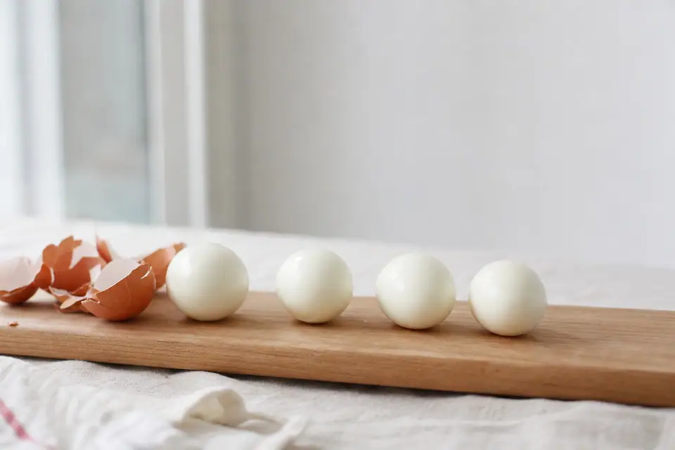 Œufs durs écalés proprement, alignés sur une planche à côté de leurs coquilles