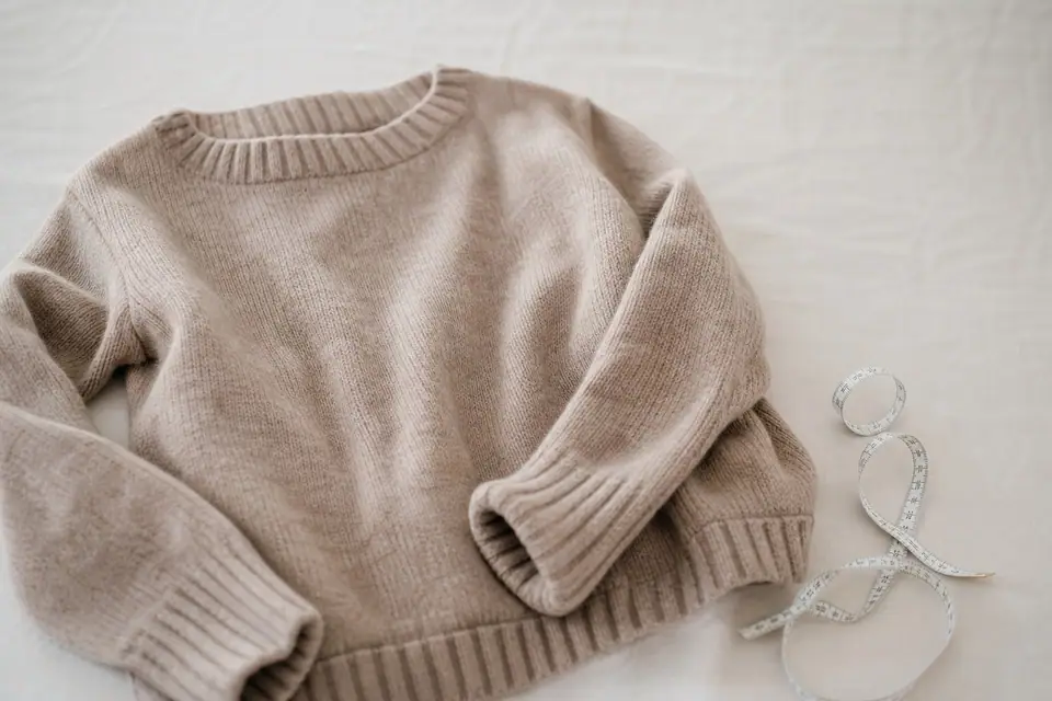 Pull en laine posé à plat sur une surface claire à côté d’un mètre ruban de couturière