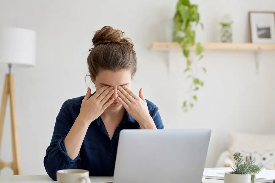 Personne se frottant les yeux devant un ordinateur portable, bureau lumineux