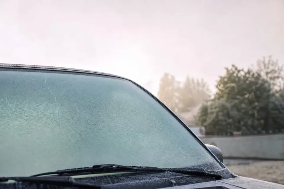 Fissure fine traversant un pare-brise de voiture recouvert de givre un matin d’hiver