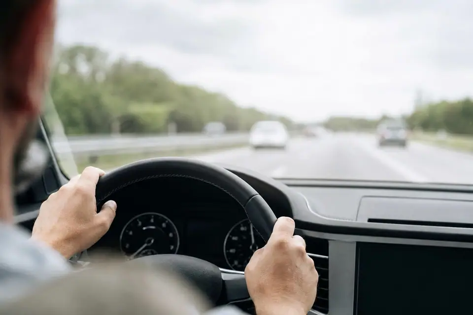 Mains posées sur un volant de voiture, compteur de vitesse visible en arrière-plan