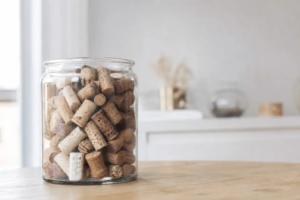 Bouchons de liège usagés rassemblés dans un bocal en verre, posés sur une table en bois