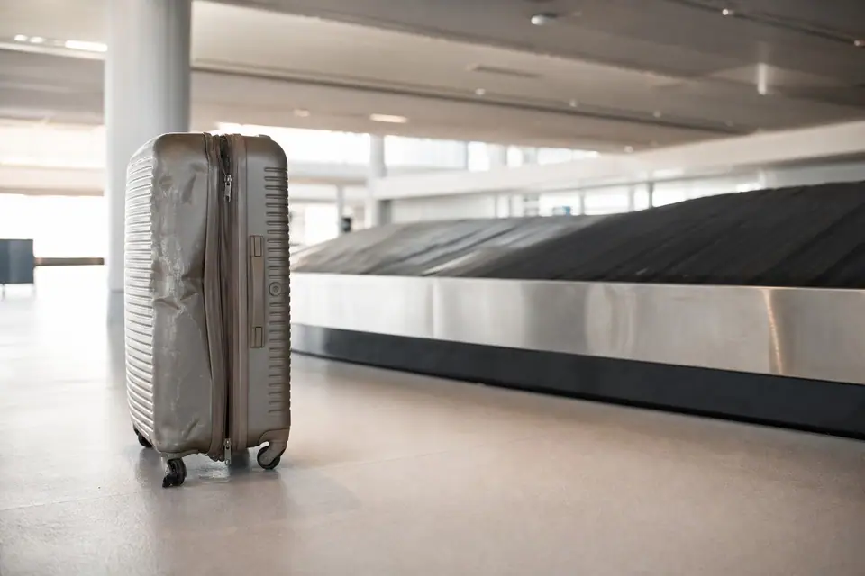 Valise cabossée avec une roulette abîmée posée près d’un tapis de récupération des bagages