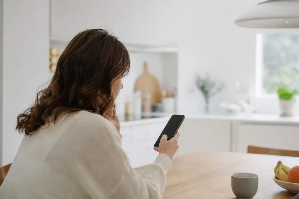 Personne consultant un relevé bancaire et un IBAN sur smartphone, table de cuisine en arrière-plan