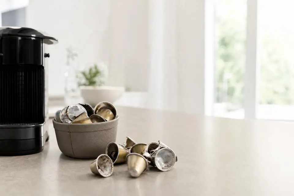 Capsules de café en aluminium usagées vidées de leur marc, posées près d’une machine